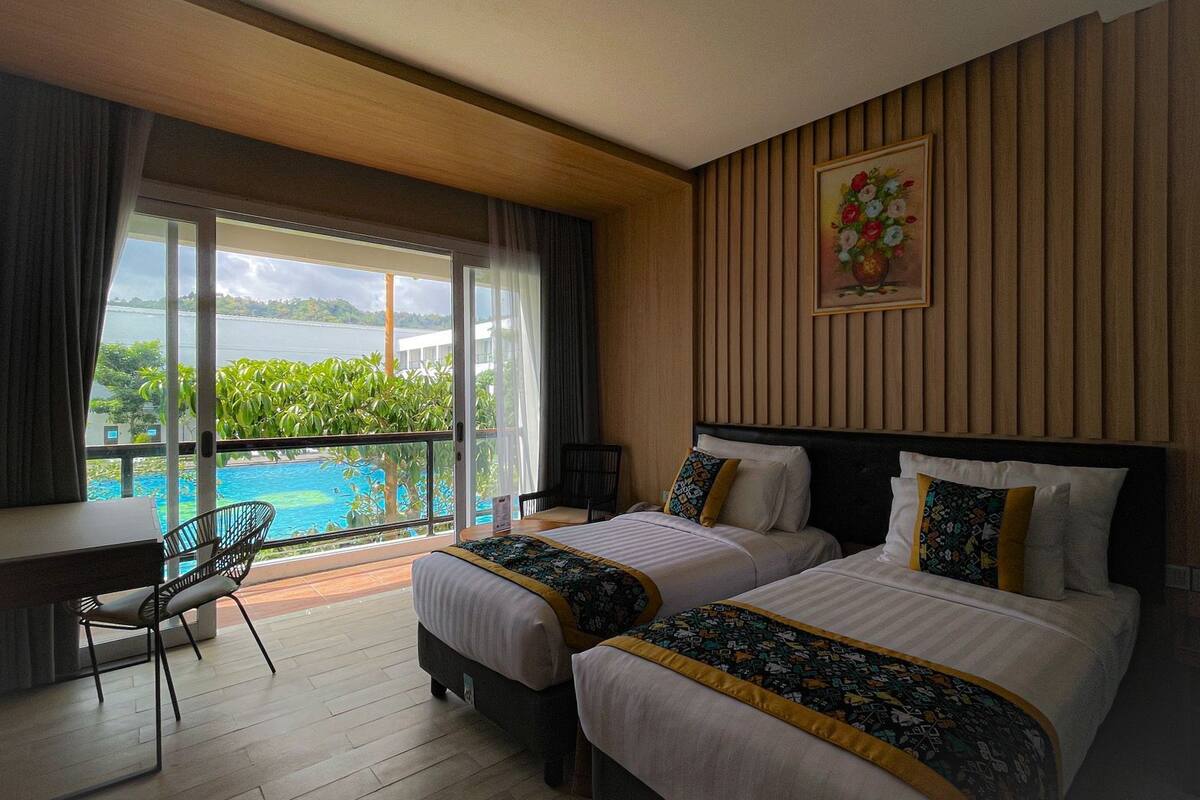 A hotel room with two beds, a desk, a chair, and a balcony with a view of a body of water.