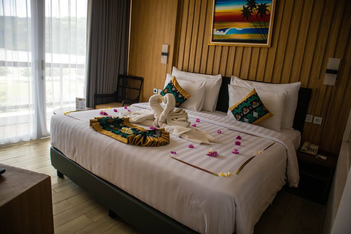 A hotel room with a bed, pillows, a chair, and a painting on the wall.