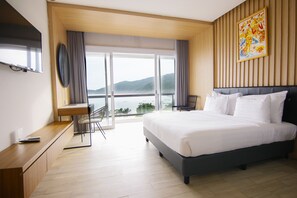 A modern hotel room with a large bed, a desk, and a view of the sea.