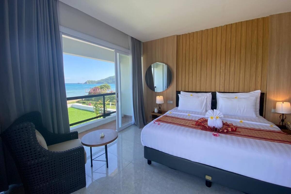 A hotel room with a large bed, a round mirror, a small table, and a view of the sea.
