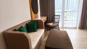 Una moderna camera d'albergo con divano, un tavolino, un poggiapiedi in vimini e una poltrona.
