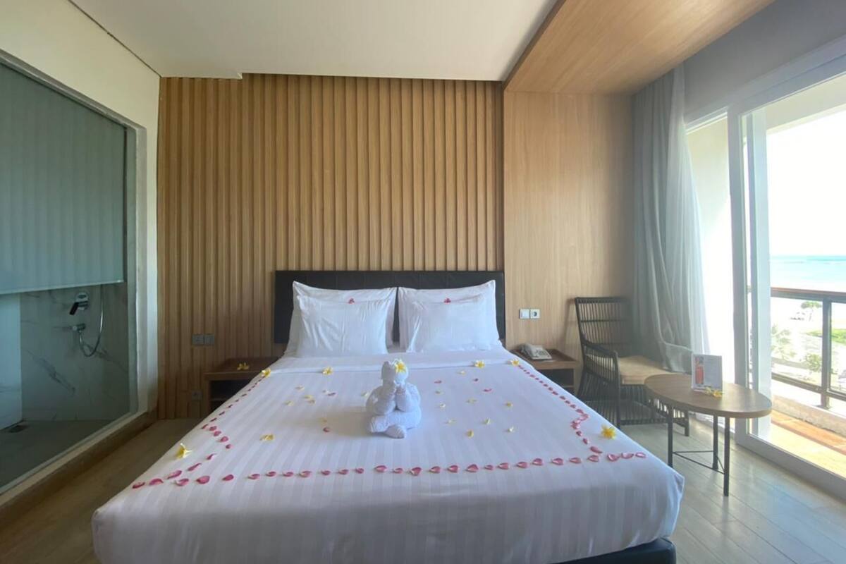 A hotel room with a bed, a small table, a chair, and a balcony with a view.