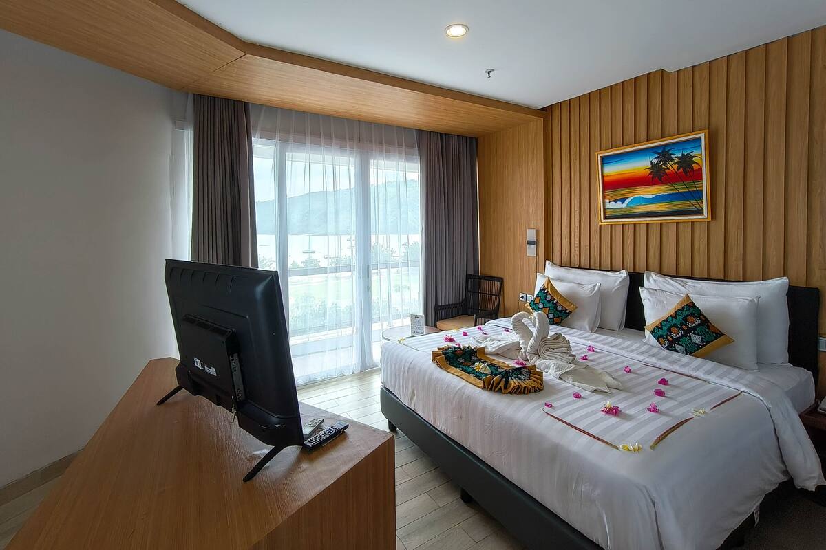 A hotel room with a bed, a desk with a computer, a chair, and a window with curtains.