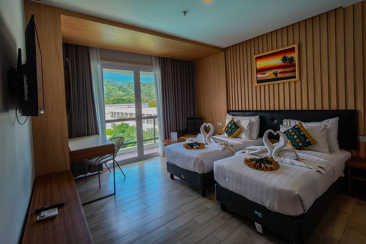 A hotel room with two beds, a TV, a balcony with curtains, and a painting of a sunset.