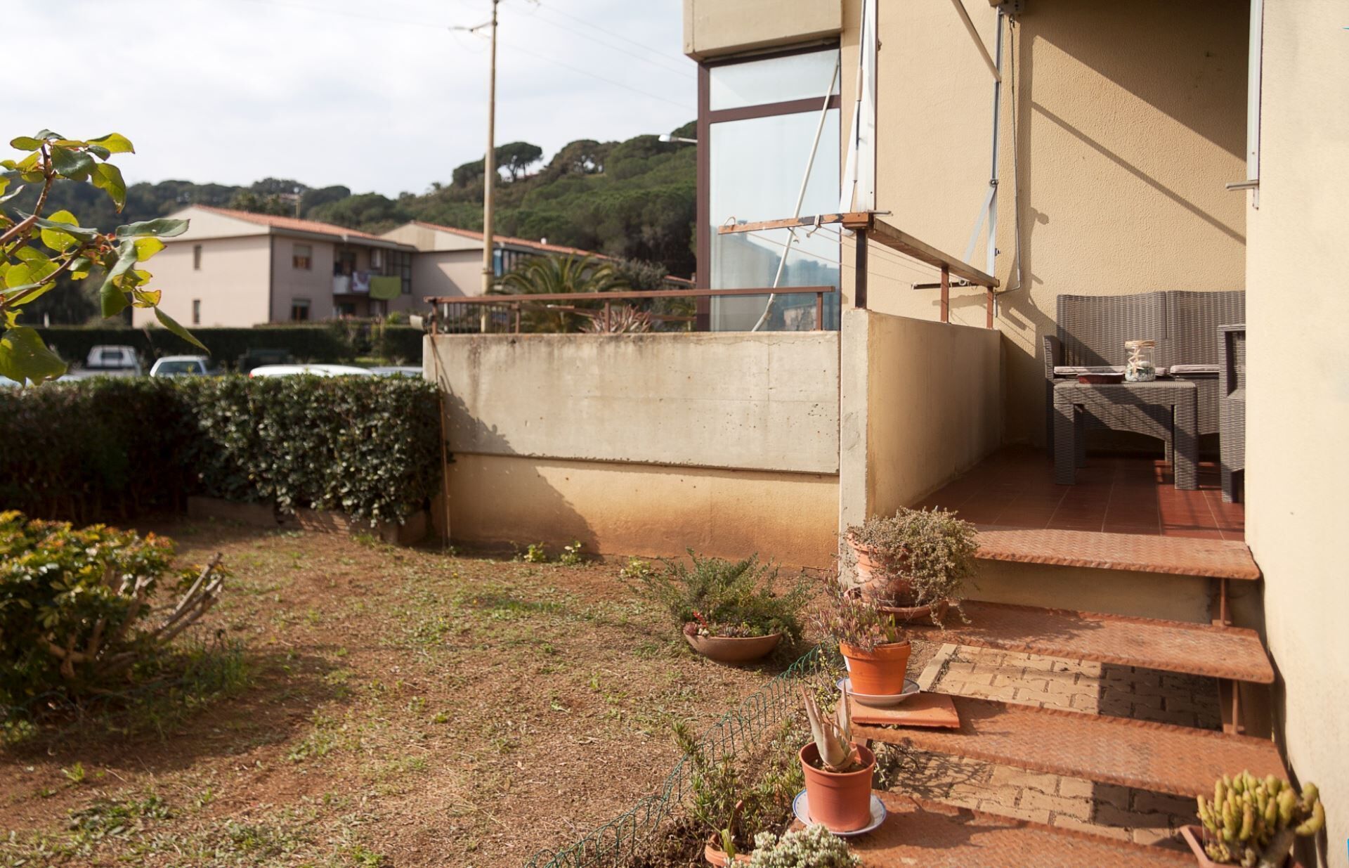 Edifici residencial amb un balcó, plantes en testos i una petita zona de seients a l'exterior.