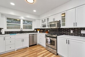 A modern kitchen with white cabinets, a stainless steel stove, and a black tiled backsplash. - Farmhouse Modern Home (Houston)
