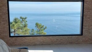 Ein Zimmer mit großem Fenster mit Meerblick, eine Couch mit Kissen und ein kleiner Tisch mit Tasse und Dekoration.