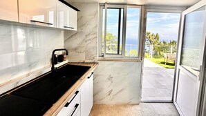 Eine moderne Küche mit einem schwarzen Herd, weißen Schränken und einem großen Fenster mit Blick auf das Meer.