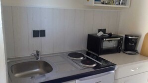Een kleine keuken met een spoelbak, fornuis, magnetron en een kleine koelkast.