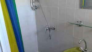 Een badkamer met een douche, een wastafel en een glazen plank.
