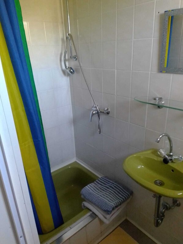 A bathroom with a shower, a sink, and a glass shelf.