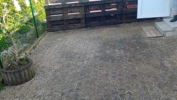 Een betegeld terras met zeshoekige tegels, een houten hekwerk en een bloempot.