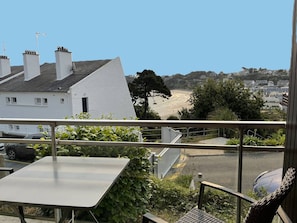 Ein Balkon mit Tisch und Stuhl mit Blick auf einen Strand und Wohnhäuser.