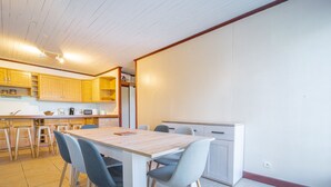 A compact kitchen with wooden cabinets, a dining table with chairs, and a small refrigerator. - Spacious 2-Star House for 10, Near Beach, with Garden and BBQ - Mimizan (Mimizan)