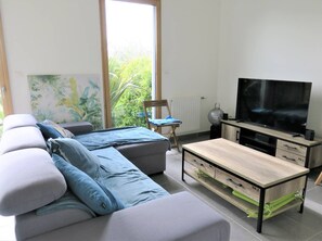Relax in this stylish living room with a sofa, coffee table, and flat-screen TV, offering a view of lush greenery outside.