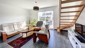 En moderne stue med sofa, sofabord og stole, en trappe og et stort vindue med udsigt.