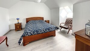 Et soveværelse med en træseng, en læderlænestol, et lille natbord i træ og en hvid loftsarmatur.