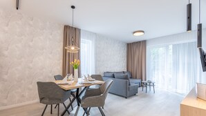 Un salon moderne avec un canapé gris, une table à manger avec des chaises et un téléviseur fixé au mur.