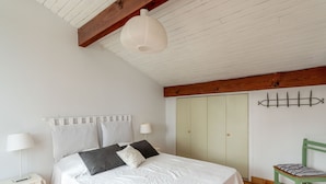 Een slaapkamer met een bed, nachtkastje, lamp, kledingkast en een stoel.