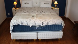 Una cama con colcha floral y dos almohadas con la etiqueta "TRIANON".