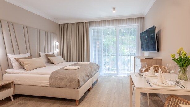 Een moderne hotelkamer met een groot bed, een zithoek met een tafel gedekt voor twee personen, en een aan de muur bevestigde televisie.