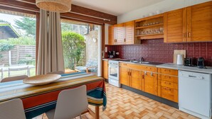 Una cocina con armarios de madera, una estufa y un lavavajillas. Hay una ventana con cortinas, una mesa con sillas y una lámpara colgante.