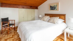 Un dormitorio con techo de madera, una cama con almohadas a rayas, una silla y un armario.
