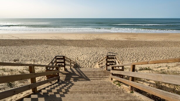 A wooden staircase leading to a sandy beach with a view of the ocean.