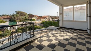 A balcony with a checkered floor, a railing, and a view of houses in the background.