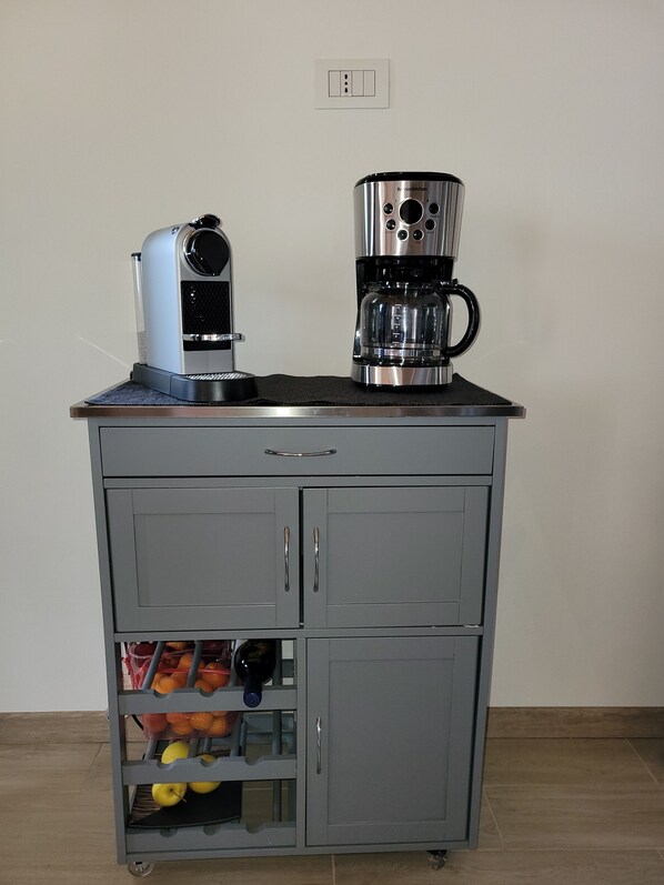 A kitchenette with a coffee maker, a kettle, and a fruit basket.
