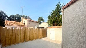 Une allée pavée mène à une zone délimitée par une barrière et entourée d’une clôture en bois.
