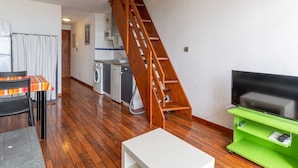 A compact living space with a wooden staircase, a kitchen area, a dining table, and a television on a stand. - Apartment with ocean view, balcony, and all comforts, in Mimizan for 6 people (Mimizan)