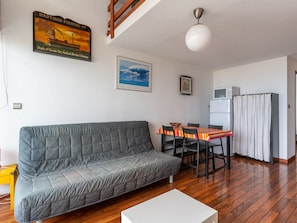 A living room with a sofa, dining table, chairs, a white coffee table, a ceiling light, a refrigerator, and a kitchen area.