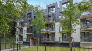 Un edificio moderno de varios pisos con balcones, rodeado de árboles y un patio amurallado.