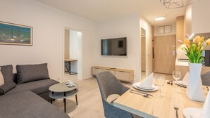Una sala moderna con un sofá, una mesa de comedor para dos personas y un televisor montado en la pared.
