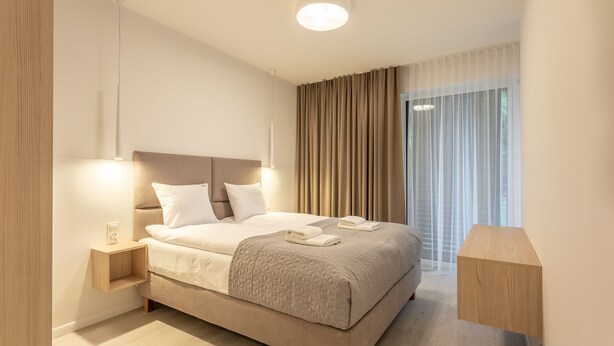 Ein modernes Hotelzimmer mit einem großen Bett, Nachttischen, einem Beistelltisch und Blick ins Freie durch große Fenster.