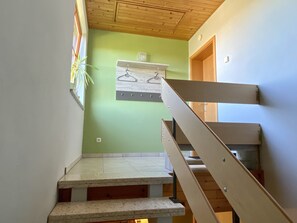 Staircase with a handrail and a door to the right, featuring a shelf with hooks.