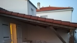 A covered patio area with a tiled floor, a table with chairs, and a door leading to an interior space. - Vacation home close to the beach (La Faute-sur-Mer)