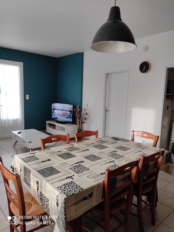A dining area with a table set for four, a television in the background, and a clock on the wall.