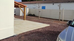 A residential area with a white building, a wooden pergola, and a gravel driveway.