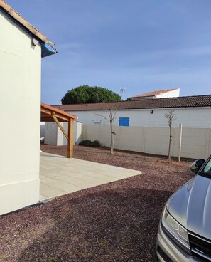 Un quartier résidentiel avec un bâtiment blanc, une pergola en bois et une allée gravillonnée.