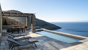 Eine Steinterrasse mit Sitzmöglichkeiten im Freien und einem Pool mit Blick auf das Meer.