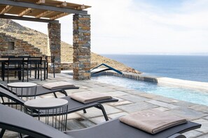 An outdoor pool area with stone pillars, lounge chairs, and a view of the sea.