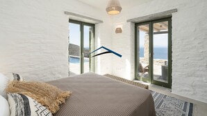 Ein Schlafzimmer mit einem Bett, einer Pendelleuchte und Meerblick durch große Fenster.