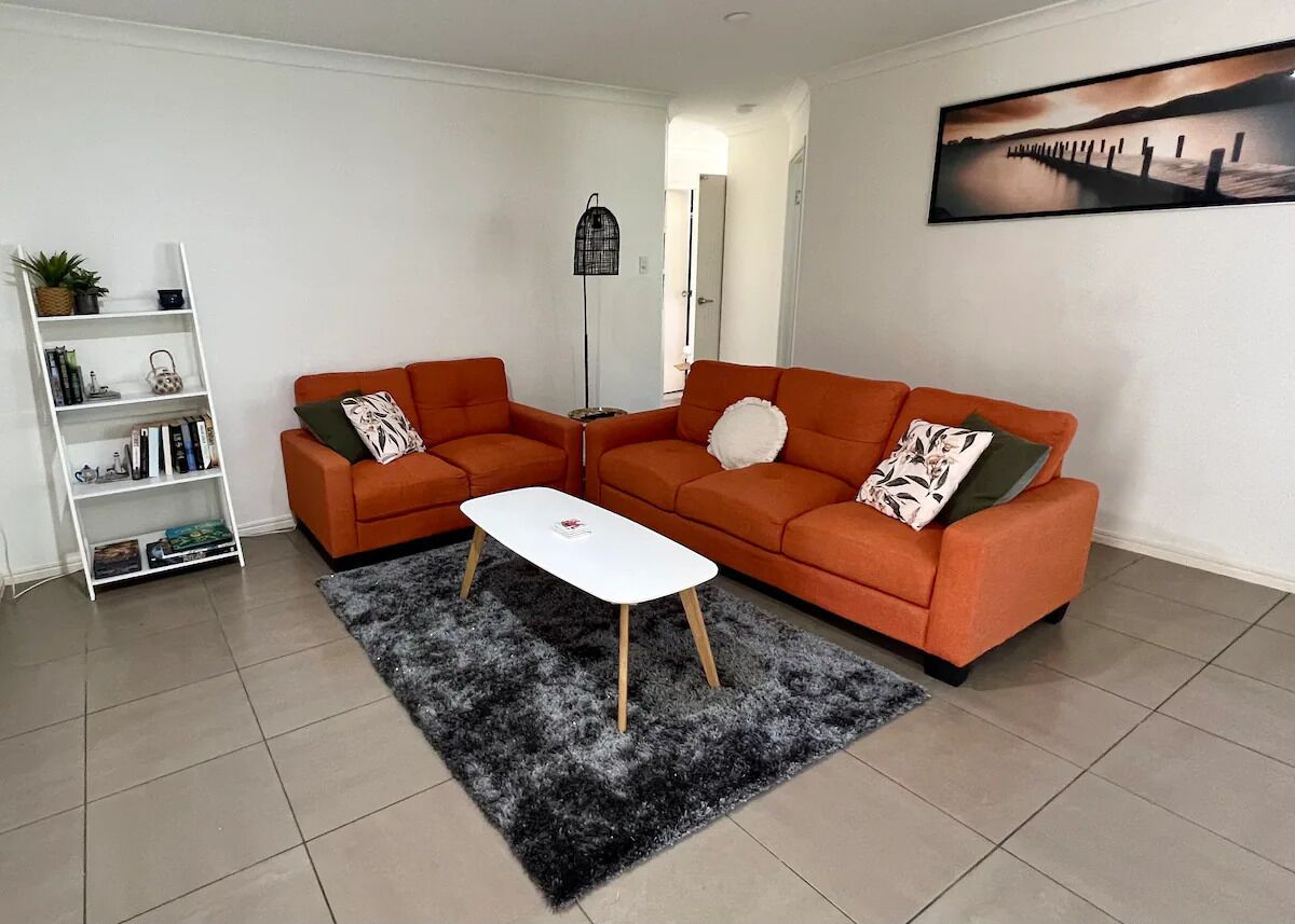 Un salon avec deux canapés orange, une table basse blanche, un tapis à poils longs noir et une bibliothèque blanche.