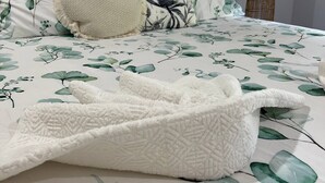 En seng med blomstret sengetæppe, et hvidt pled og en beige pude.
