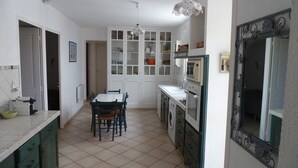 Une cuisine compacte avec des meubles blancs, une table à manger avec des chaises, un lave-linge et un four ancien.