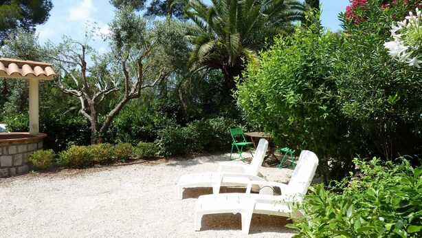 Une terrasse de jardin avec deux chaises longues blanches, une pergola en pierre et une végétation luxuriante.