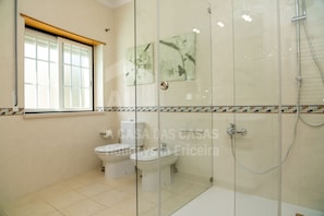 A bathroom with a toilet, bidet, and glass-enclosed shower area. - Villa BelaVista by ACasaDasCasas (Ericeira)
