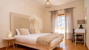 Une chambre moderne avec un grand lit, une table de chevet avec une lampe, un bureau avec une chaise et une fenêtre avec des rideaux.